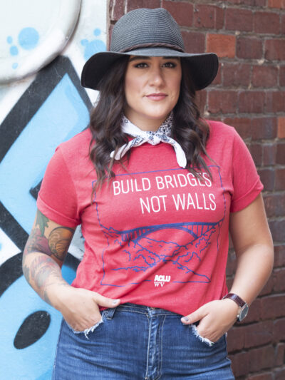 Model is pictured wearing a red Build Bridges Not Walls Tee Shirt showing the New river Gorge Bridge