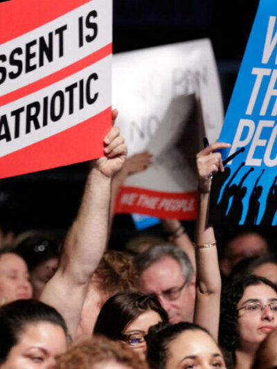 ACLU supporters hold signs that say "DISSENT IS PATRIOTIC" and "WE THE PEOPLE"