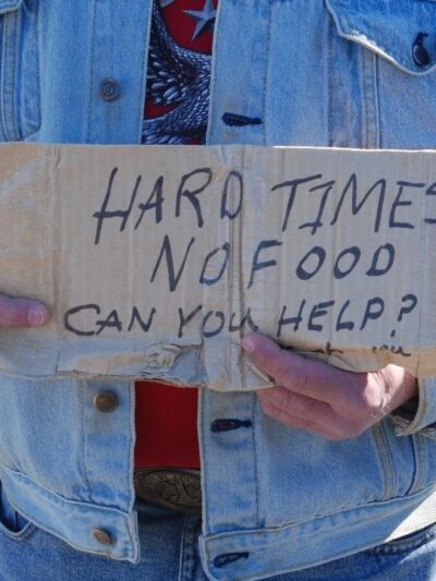 A person holds a sign that says Hard Times, No Food, Can you help?