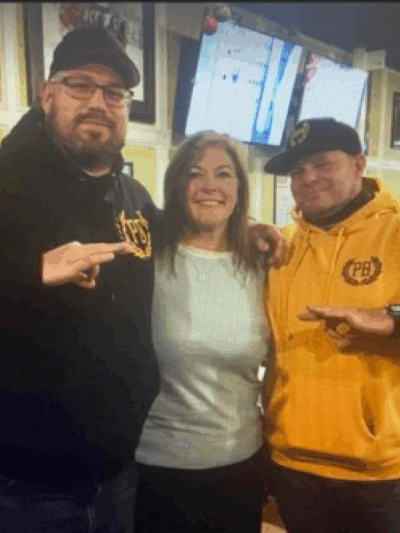 A Jackson County Commissioner stands between two men wearing Proud Boys-branded clothing as the men flash white power signs with their hands