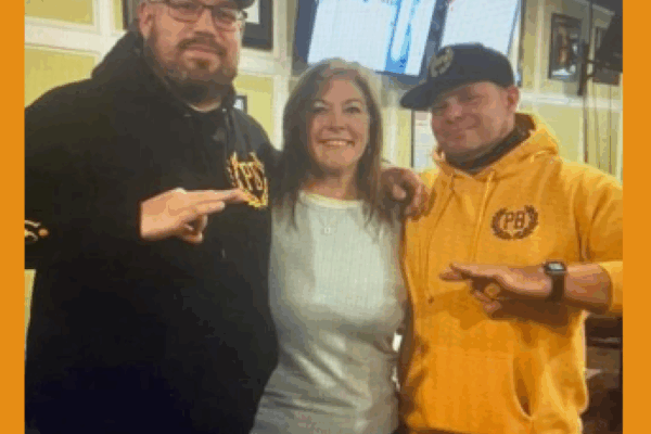 A Jackson County Commissioner stands between two men wearing Proud Boys-branded clothing as the men flash white power signs with their hands