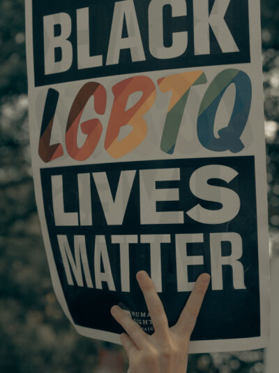a hand holds a sign reading "Black LGBTQ Lives Matter"
