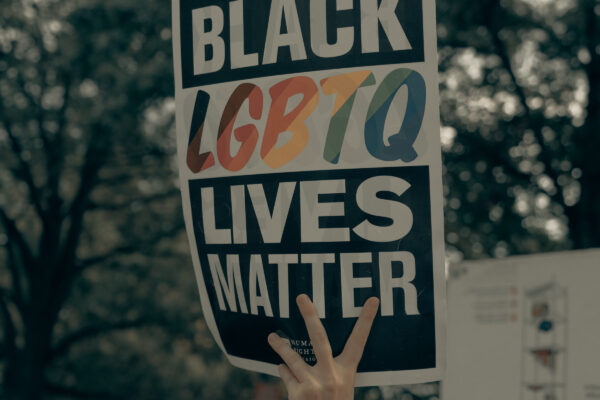 a hand holds a sign reading "Black LGBTQ Lives Matter"