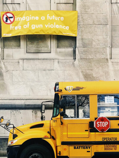 A school bus parked in front of a building carrying a yellow sign that says "Imagine a world free of gun violence."