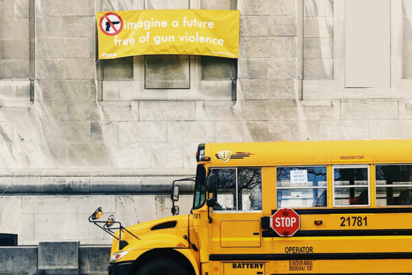 A school bus parked in front of a building carrying a yellow sign that says "Imagine a world free of gun violence."