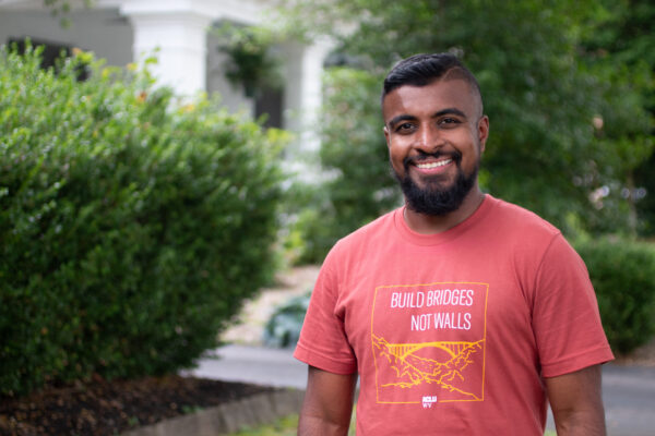 Kasun Wijayagurusinghe is pictured in an orange Build Bridges Not Walls tee shirt in front of the ACLU-WV Charleston Office