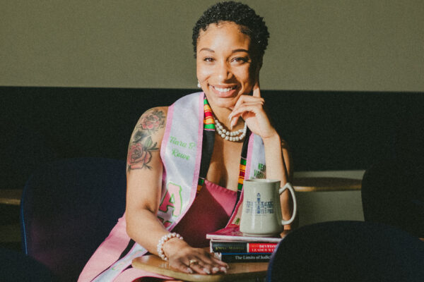 Tiara Rowe is a young Black women with short hair and a shoulder tattoo sits at a table with books and a coffee mug