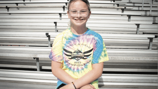 Becky Pepper Jackson sits on bleachers at her school wearing a tie-dyed shirt and glasses.