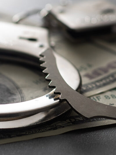 Handcuffs are shown with 100 dollar bills to symbolize the cash bail system