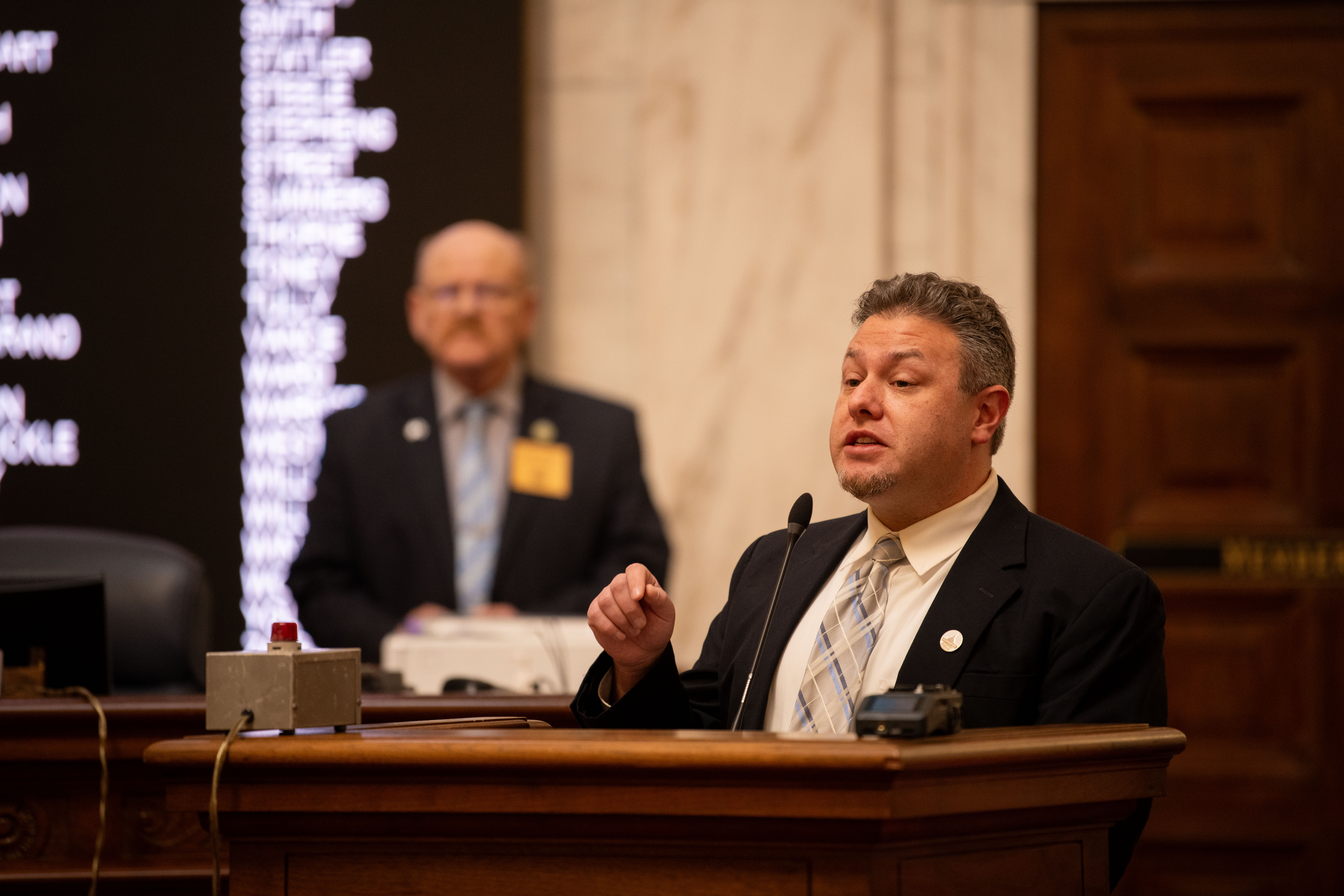 Eli Baumwell, a white man in a dark suit, speaks at a podium.