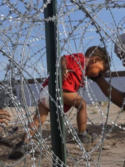 A young child in a red shirt tries to make their way through razor wire.