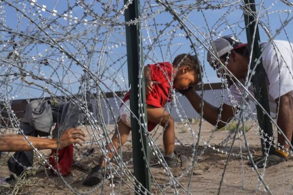 A young child in a red shirt tries to make their way through razor wire.