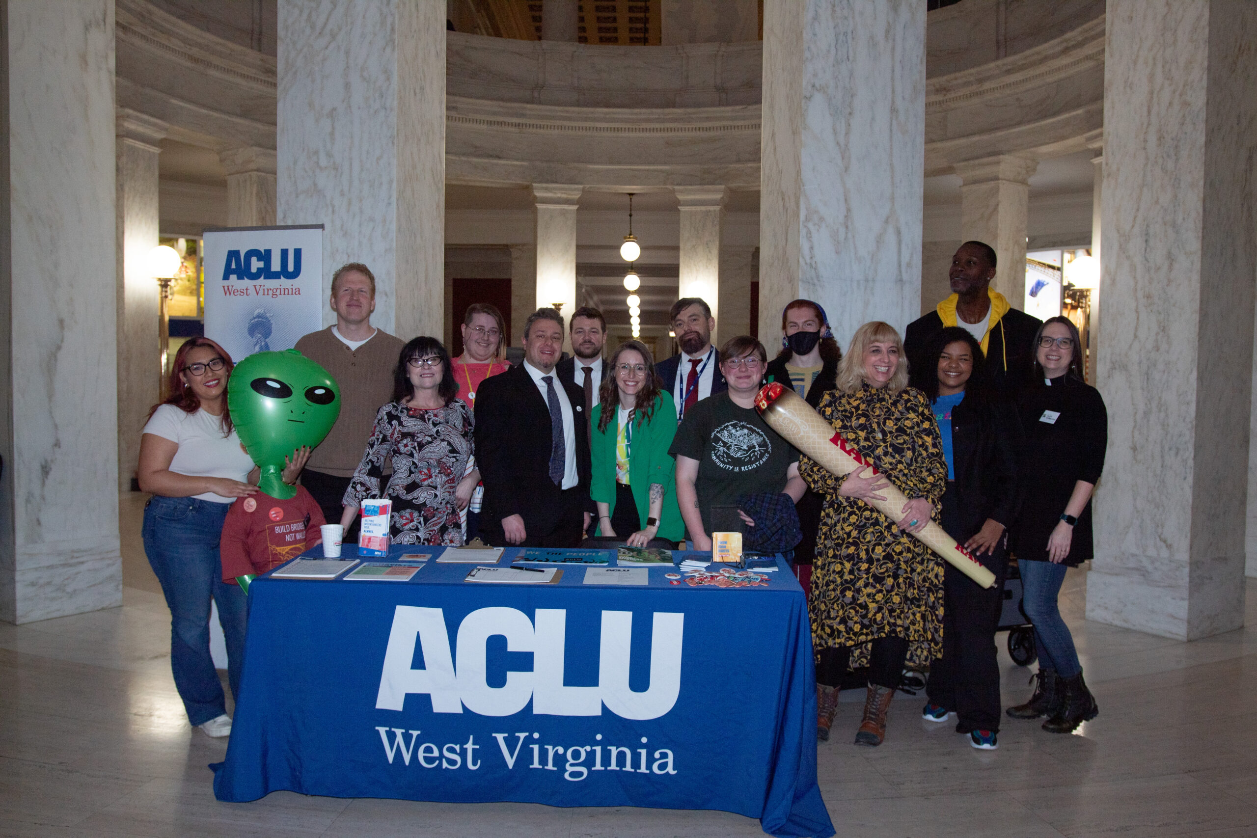 The staff of ACLu-WV gather behind the Lobby Day registration table draped in an ACLU of West Virginia tablecloth.