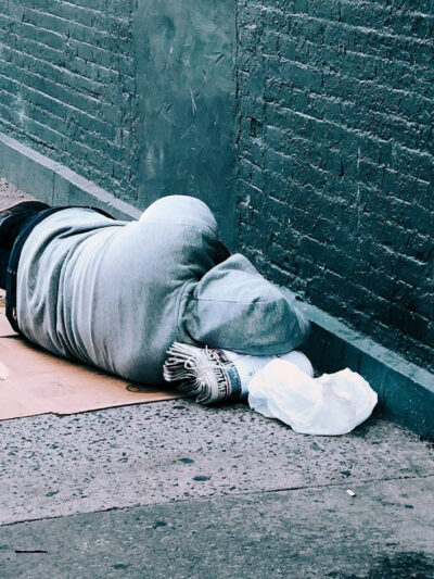 Turned away from the camera, a person sleeps on the street next to a brick wall