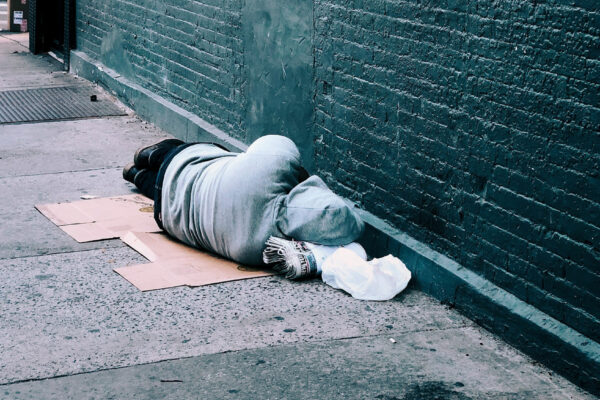 Turned away from the camera, a person sleeps on the street next to a brick wall