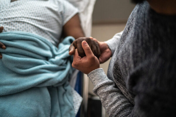 A person holds the hand of another person who is in a hospital bed.