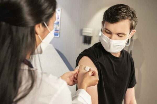 A person wearing a mask is given a shot by a doctor.