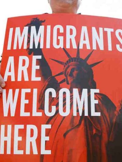 People hold up signs with the Statue of Liberty and the words "IMMIGRANTS ARE WELCOME HERE"