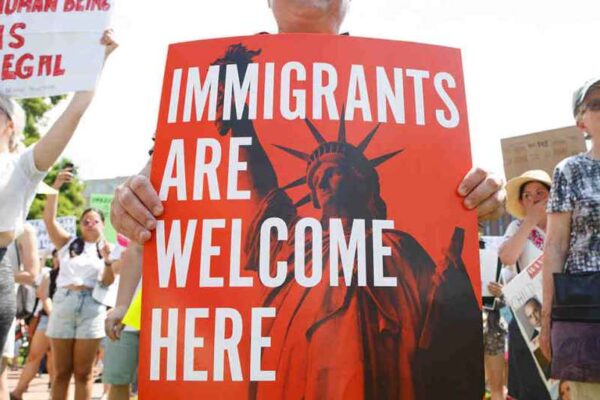 People hold up signs with the Statue of Liberty and the words "IMMIGRANTS ARE WELCOME HERE"