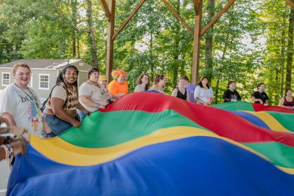 Campers at the 2025 camp take part in a group exercise with a giant rainbow flag