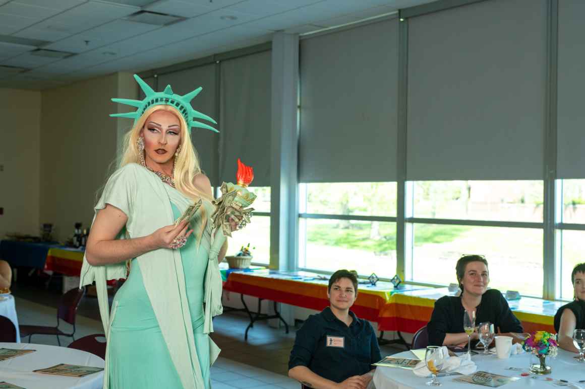 A drag performer dressed as Lady Liberty preforms a number for an audience. 