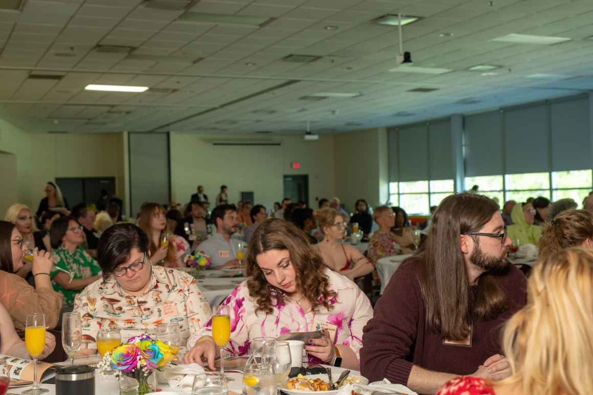 Attendees sit at tables and read the program while listening to speeches. 