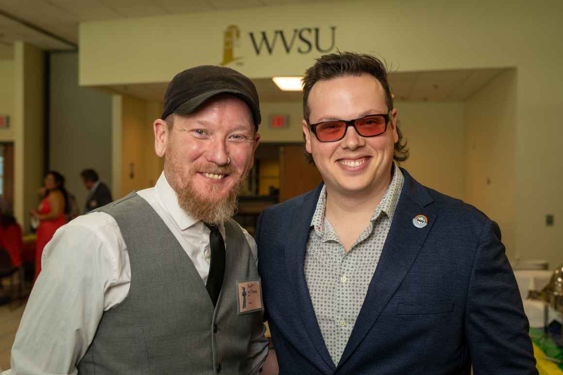 A man in a grey vest and and another man in a blue jacket pose for a picture.