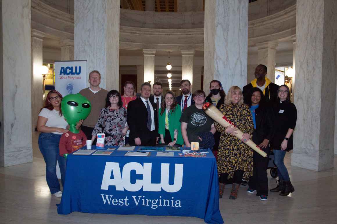 The staff of ACLu-WV gather behind the Lobby Day registration table draped in an ACLU of West Virginia tablecloth. 