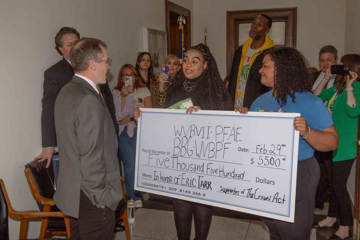 Staff members present a giant ceremonial check in honor of Senator Eric Tarr to Black women-led organizations.