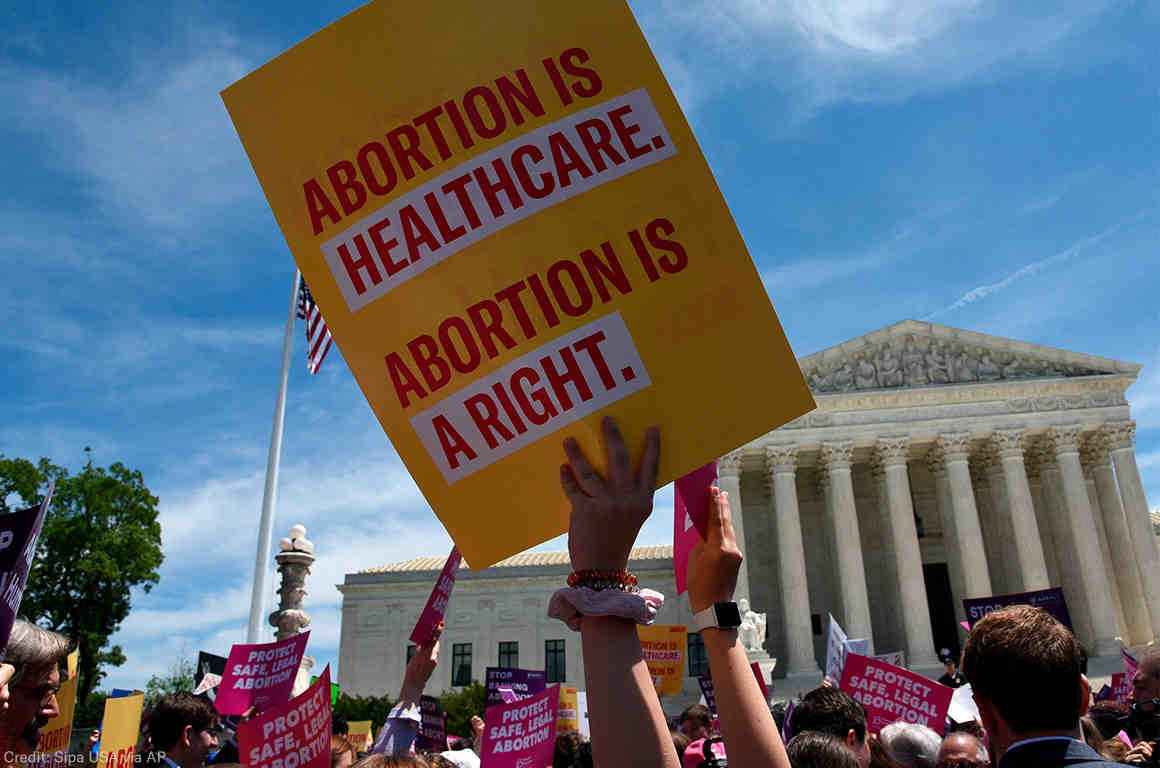 An ACLU sign reading Abortion is Healthcare. Abortion is a right. is waved in front of the U.S. Supreme Court