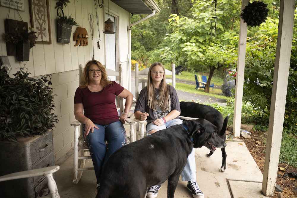 Becky Pepper-Jackson and mother, Heather Jackson, are seen on their front porch in white rocking chairs with two black lab dogs. 