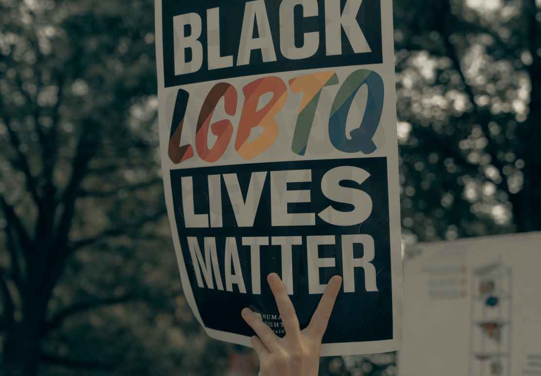 a hand holds a sign reading "Black LGBTQ Lives Matter"