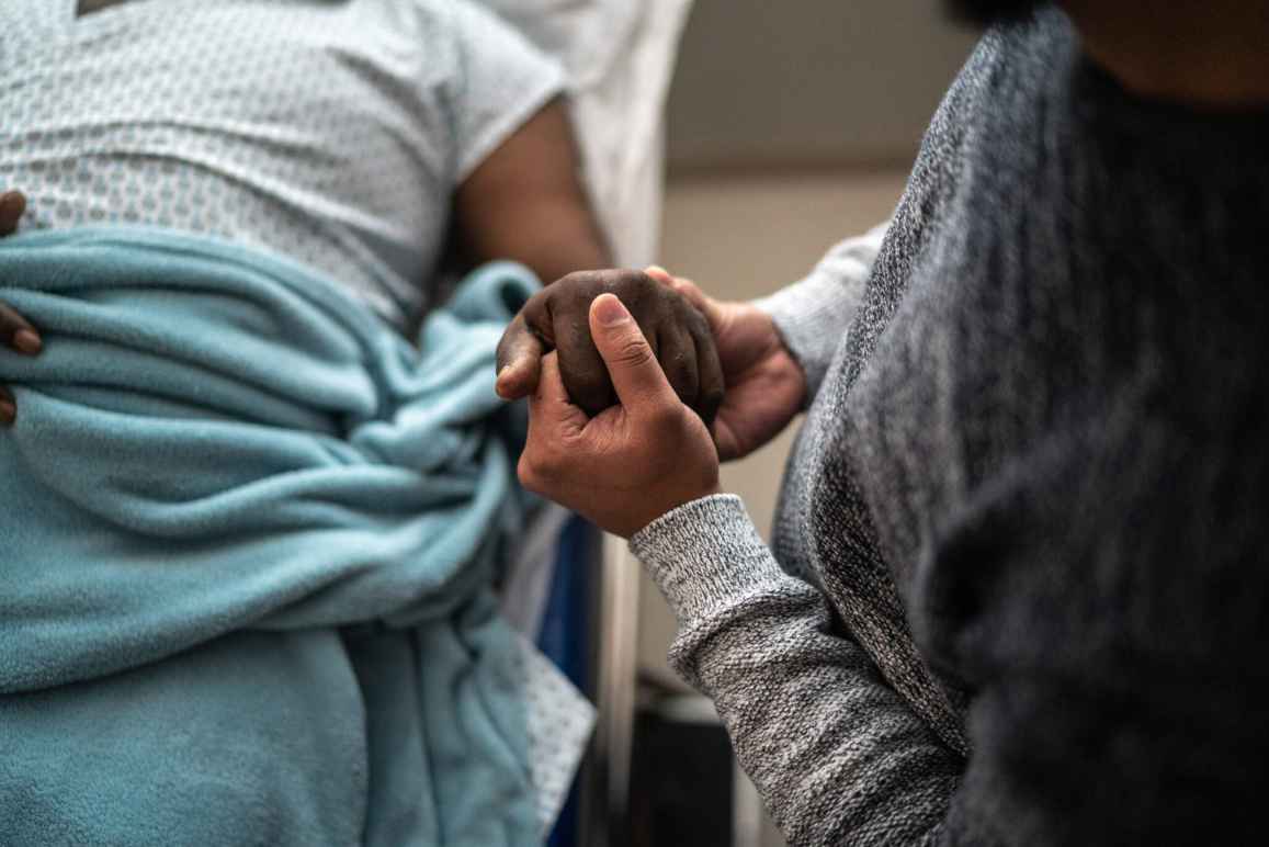 A person holds the hand of another person who is in a hospital bed. 