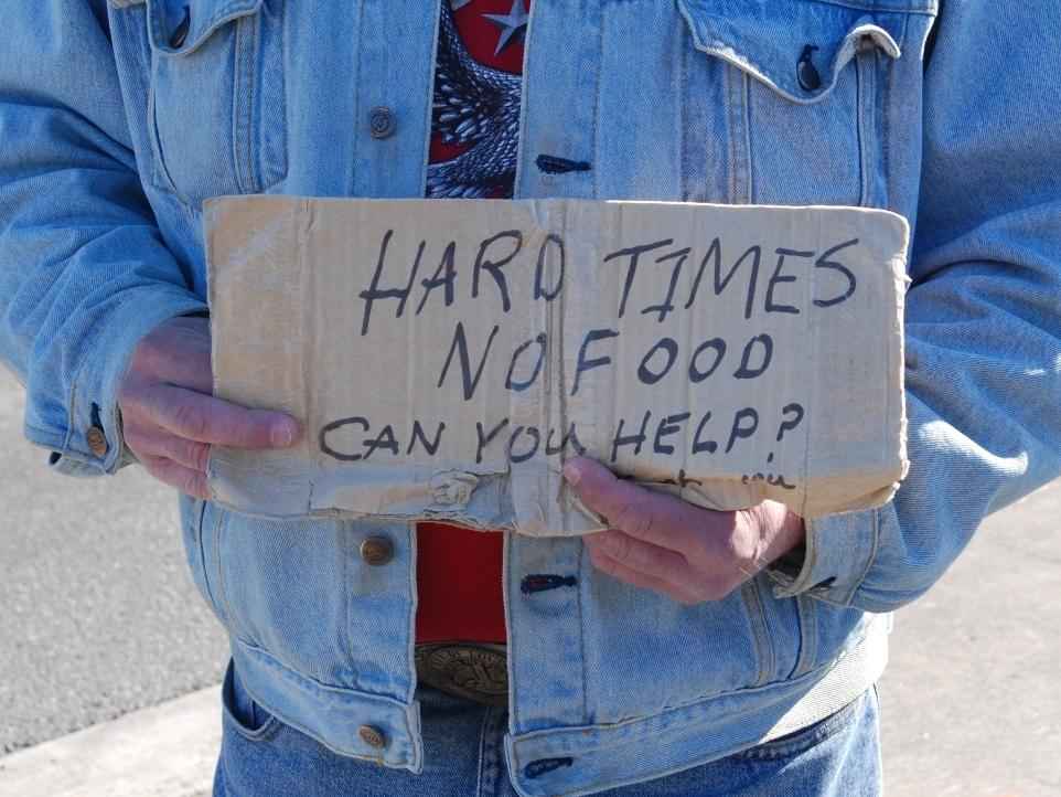 A person holds a sign that says Hard Times, No Food, Can you help?