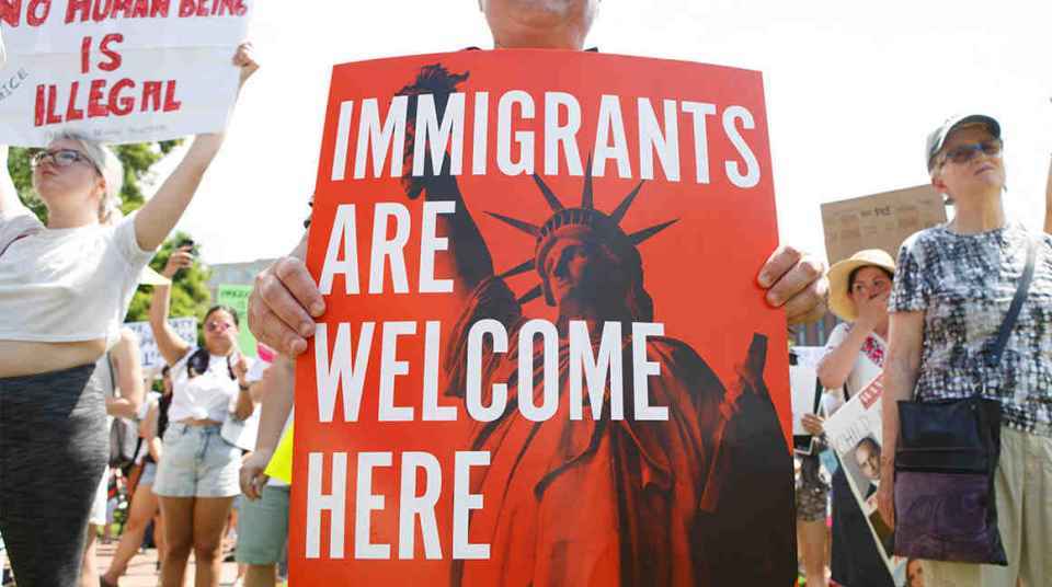 People hold up signs with the Statue of Liberty and the words "IMMIGRANTS ARE WELCOME HERE"