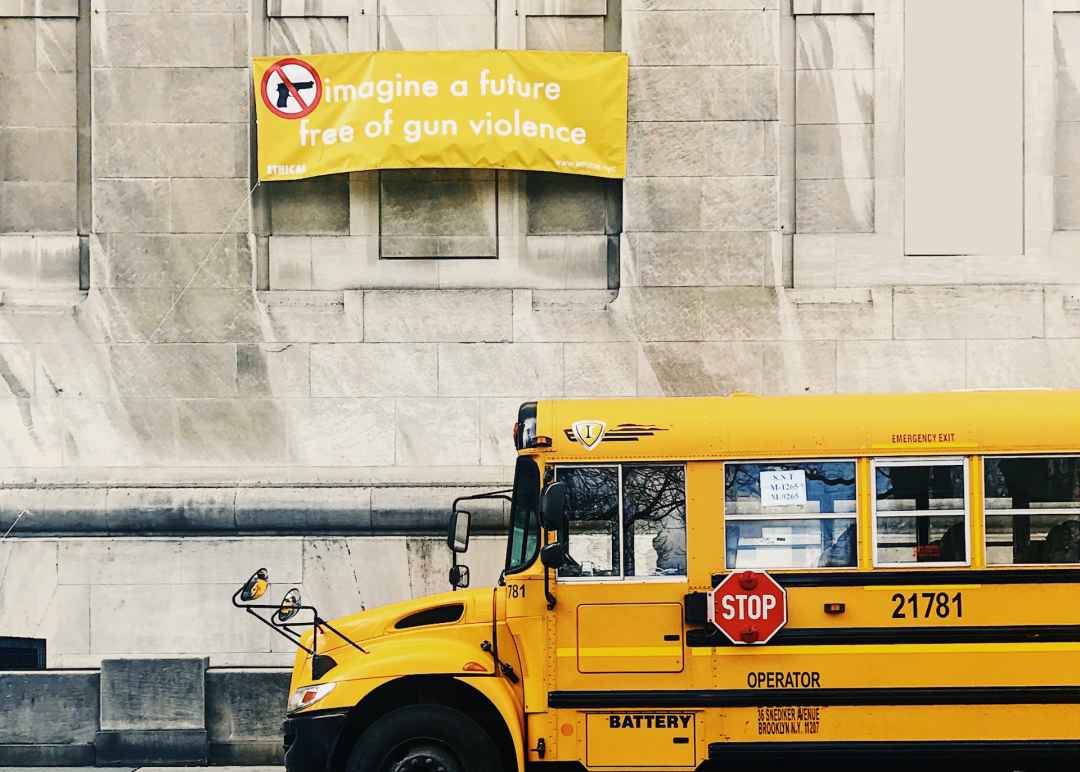 A school bus parked in front of a building carrying a yellow sign that says "Imagine a world free of gun violence."