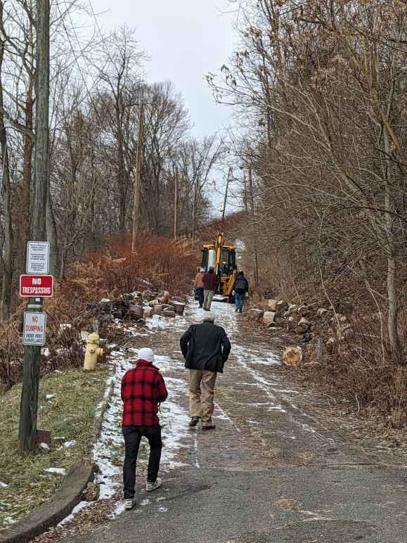 A bulldozer makes its way up a hill to an encampment as people follow behind