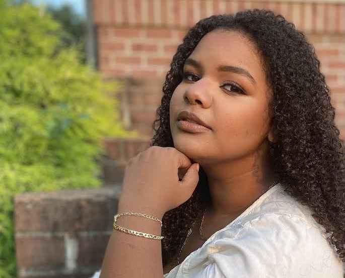 Oceanna Smith, a Black woman wearing a white top with long hair, poses for a headshot