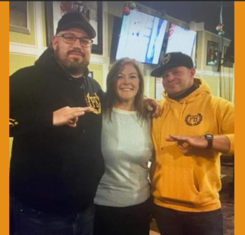 A Jackson County Commissioner stands between two men wearing Proud Boys-branded clothing as the men flash white power signs with their hands