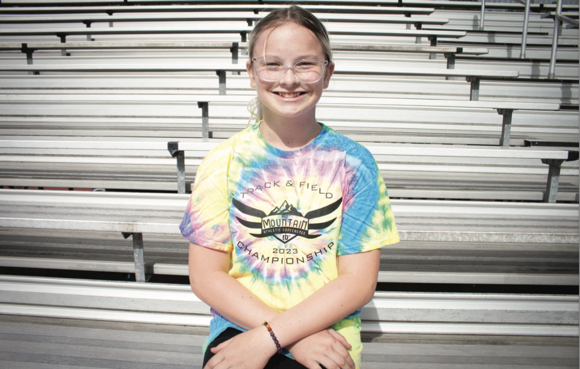 Becky Pepper Jackson sits on bleachers at her school wearing a tie-dyed shirt and glasses.