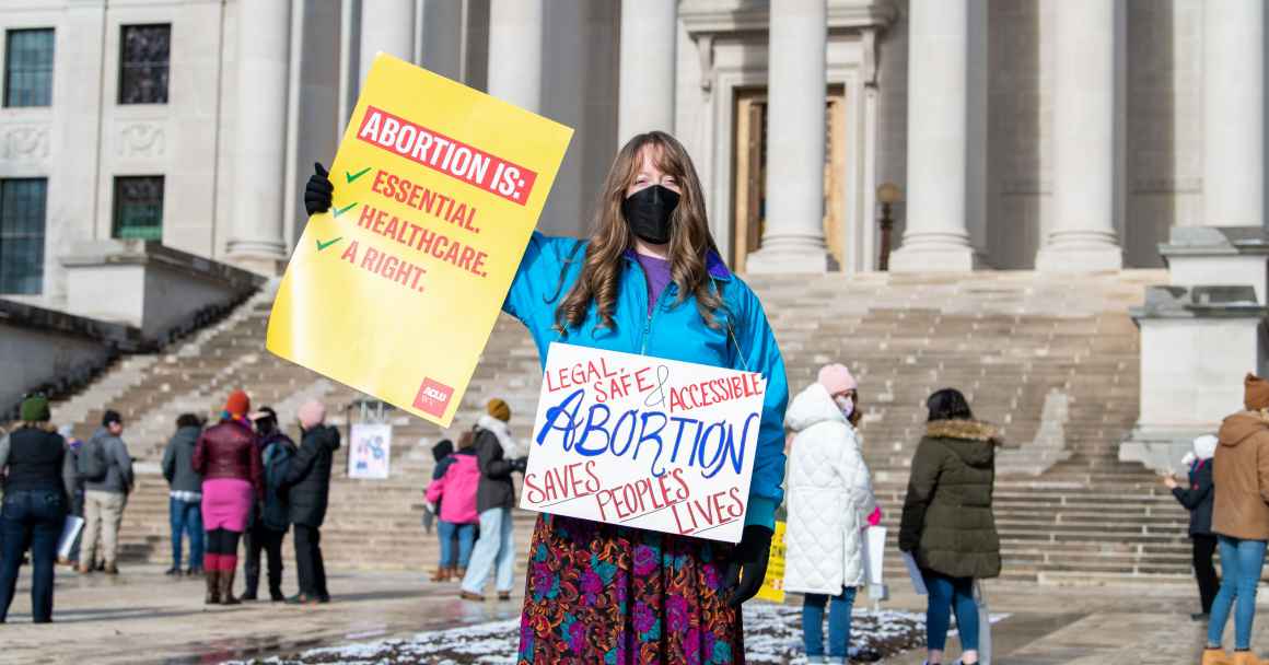 A protester holds signs saying "Abortion is: healthcare, essential, a right" 