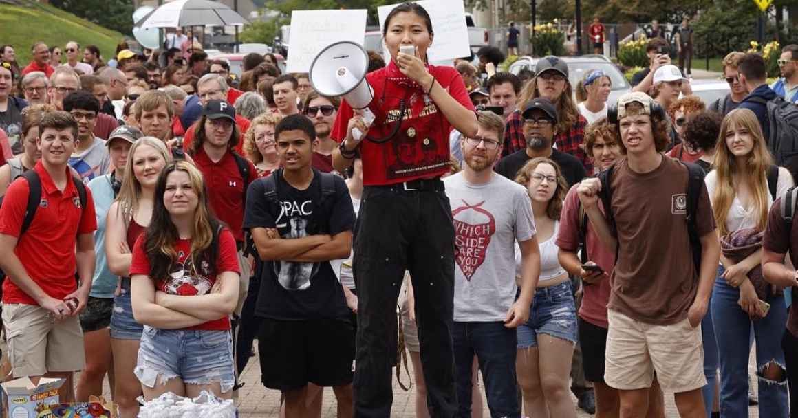 Mailyn Sadler, young Asian woman with long dark hair wearing a red shit and black pants leads a group of college students in a protest while holding a white megaphone