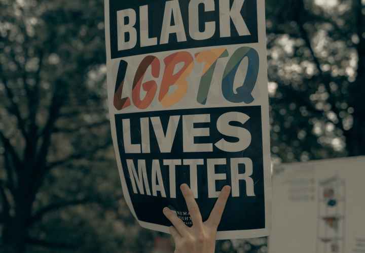 a hand holds a sign reading "Black LGBTQ Lives Matter"