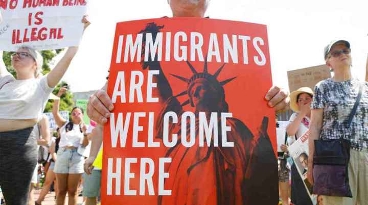 People hold up signs with the Statue of Liberty and the words "IMMIGRANTS ARE WELCOME HERE"
