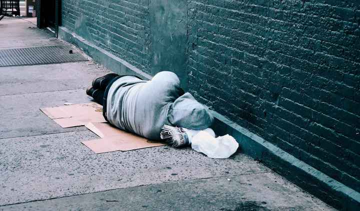 Turned away from the camera, a person sleeps on the street next to a brick wall