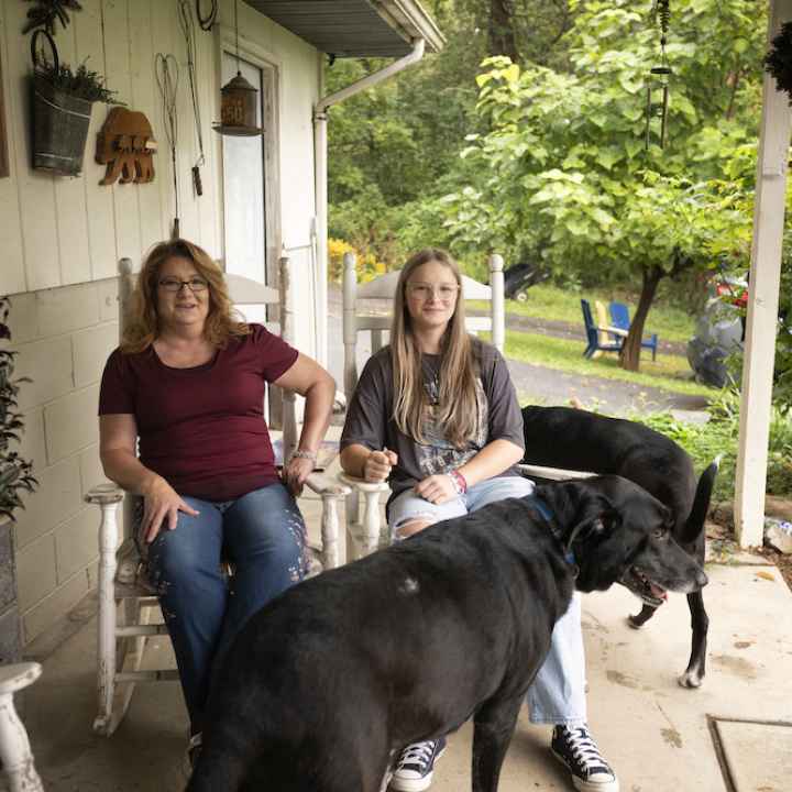 Becky Pepper-Jackson and mother, Heather Jackson, are seen on their front porch in white rocking chairs with two black lab dogs. 