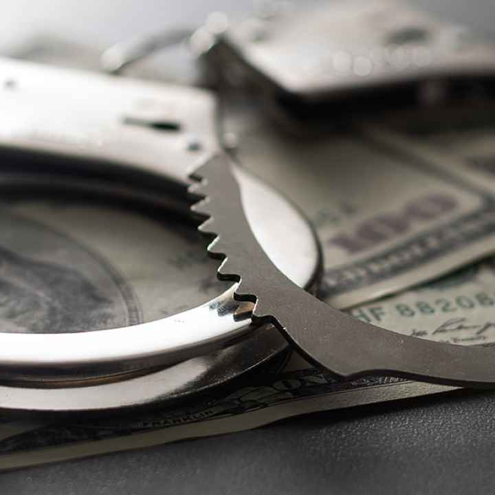 Handcuffs are shown with 100 dollar bills to symbolize the cash bail system