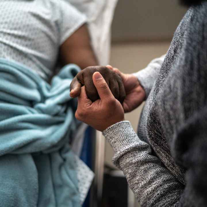 A person holds the hand of another person who is in a hospital bed.