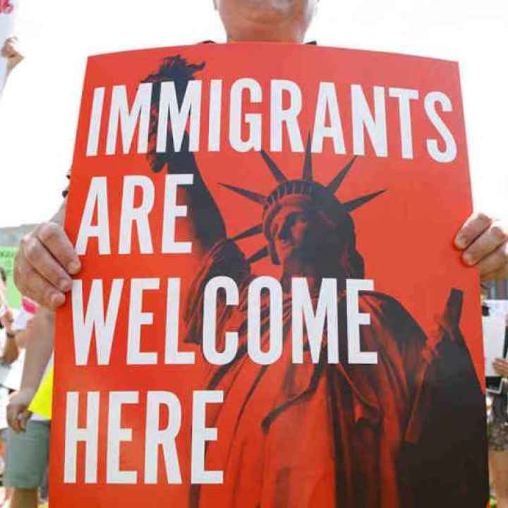 People hold up signs with the Statue of Liberty and the words "IMMIGRANTS ARE WELCOME HERE"