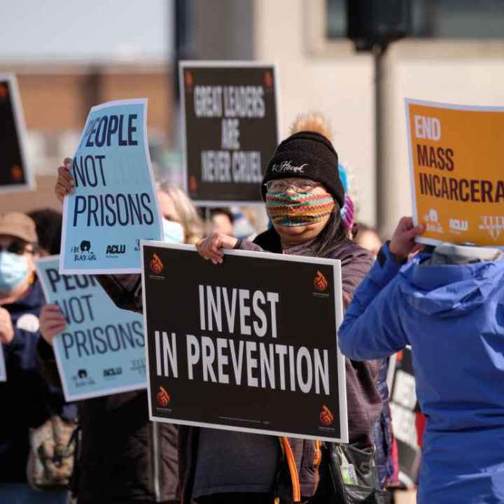 Protesters wave signs saying "INVEST IN PREVENTION," "PEOPLE NOT PRISONS," AND "END MASS INCARCERATION."